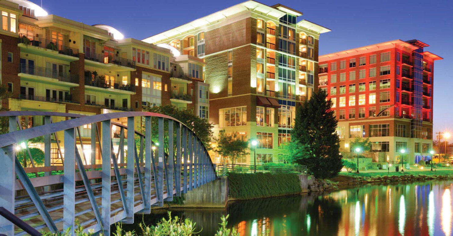 Nighttime bridge over river with cityscape in background in Greenville, South Carolina.